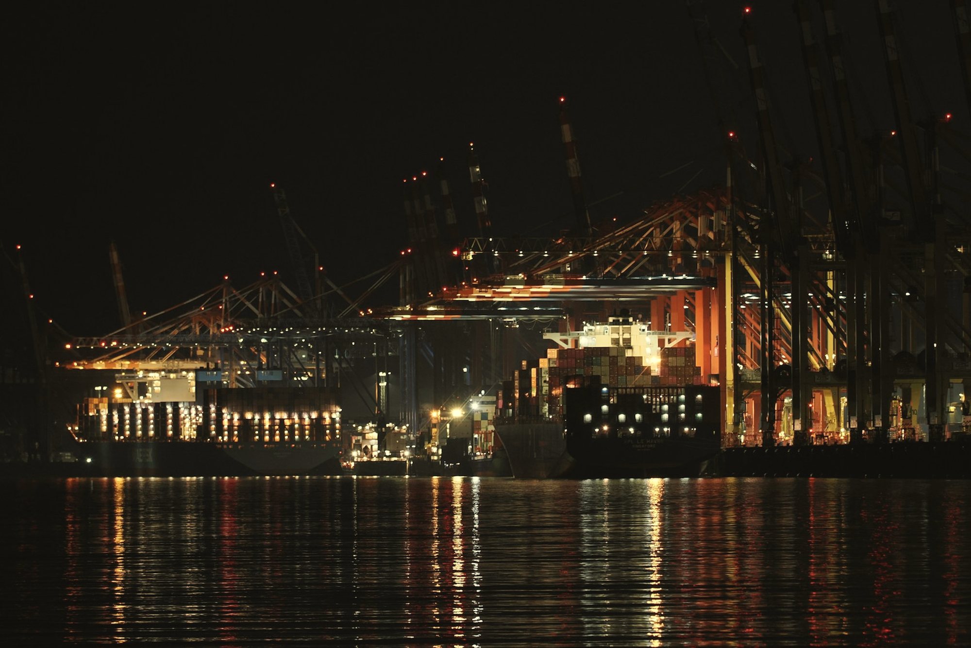A container port lit at night, reflected in the water